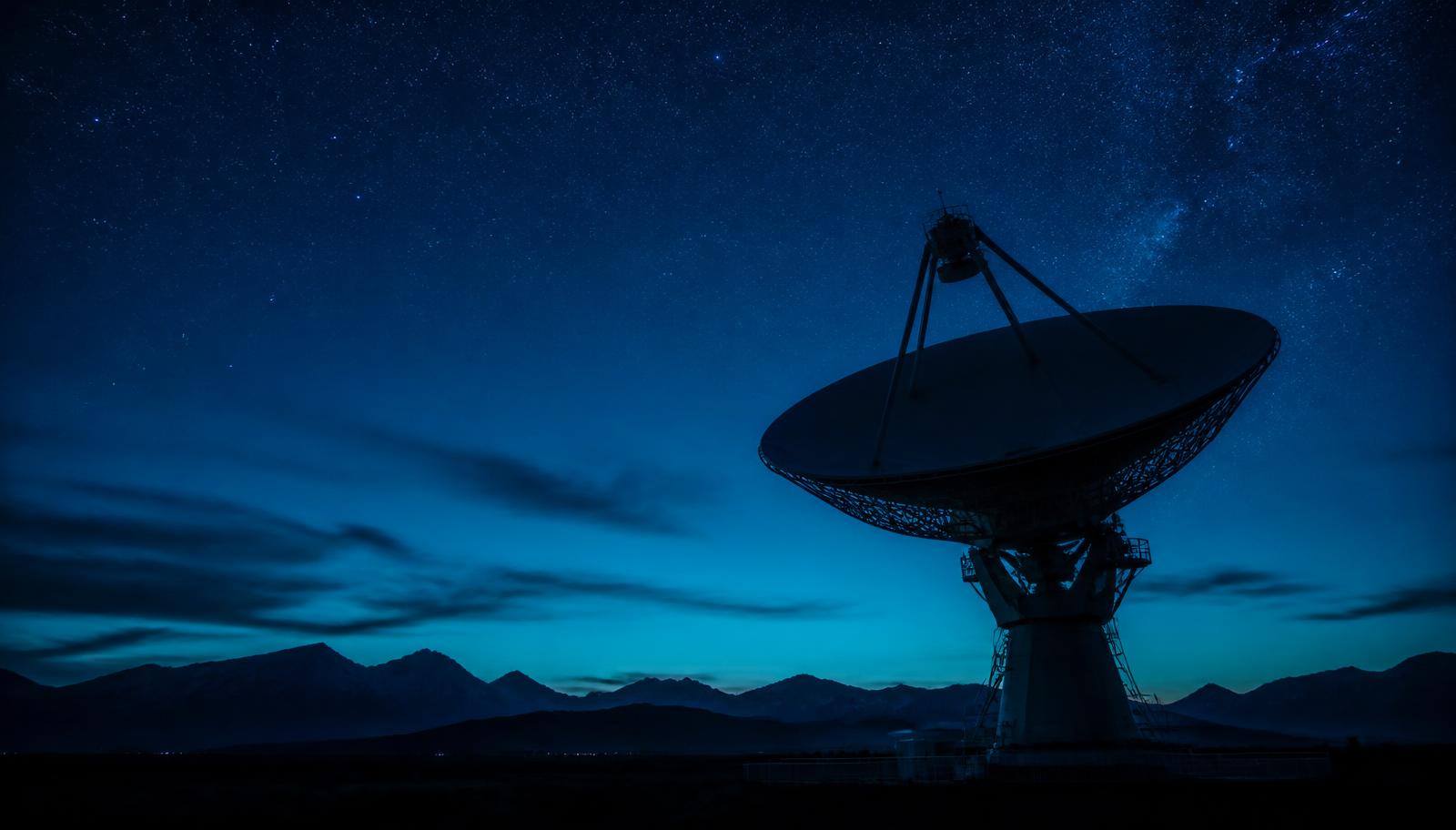 Satellite ground station dish under a star-filled night sky